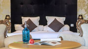Una habitación de hotel con una cama, dos lámparas, una mesa con un libro y una botella, y una flor decorativa.