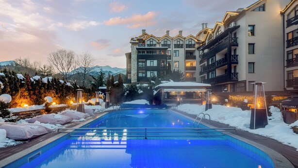 A hotel with a swimming pool surrounded by snow, featuring modern architecture and a mountain backdrop.