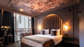 A bedroom with a large bed, a curved headboard, a ceiling mural, and a view of the outdoors.