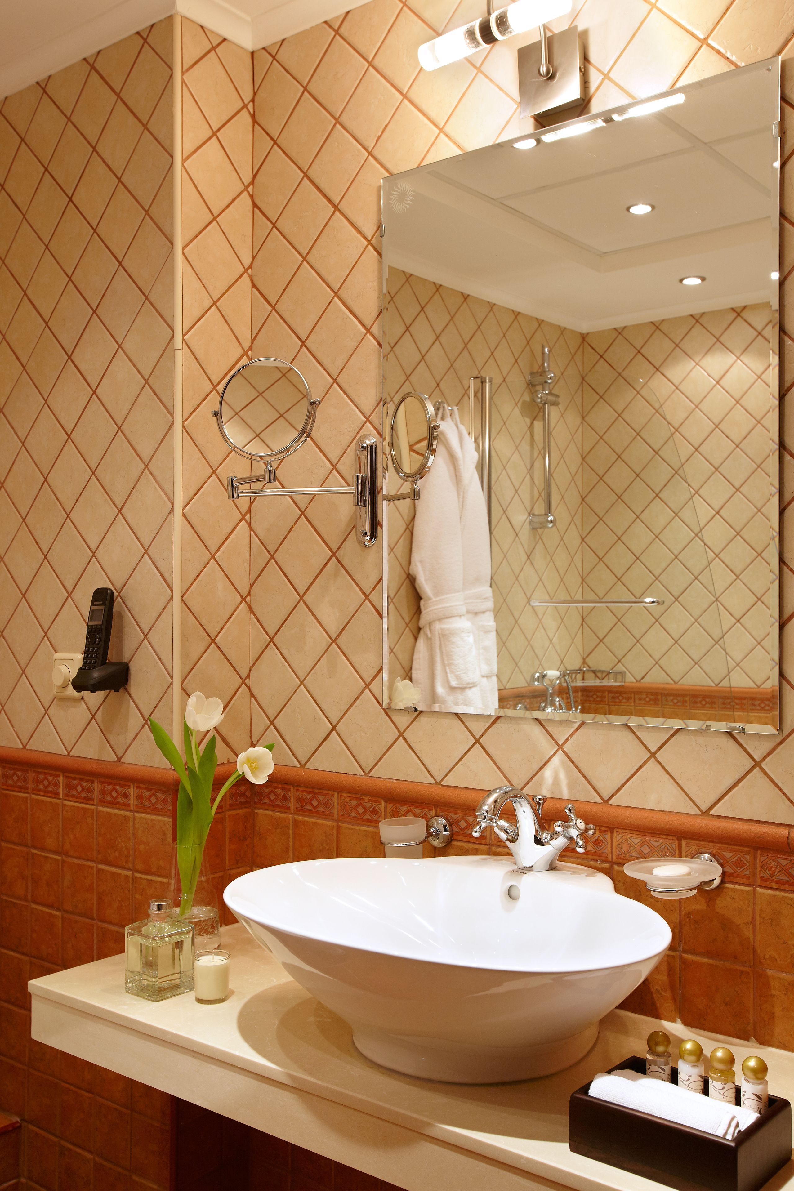 A bathroom with a large oval sink, a mirror, a towel rack, and a small vase with flowers.