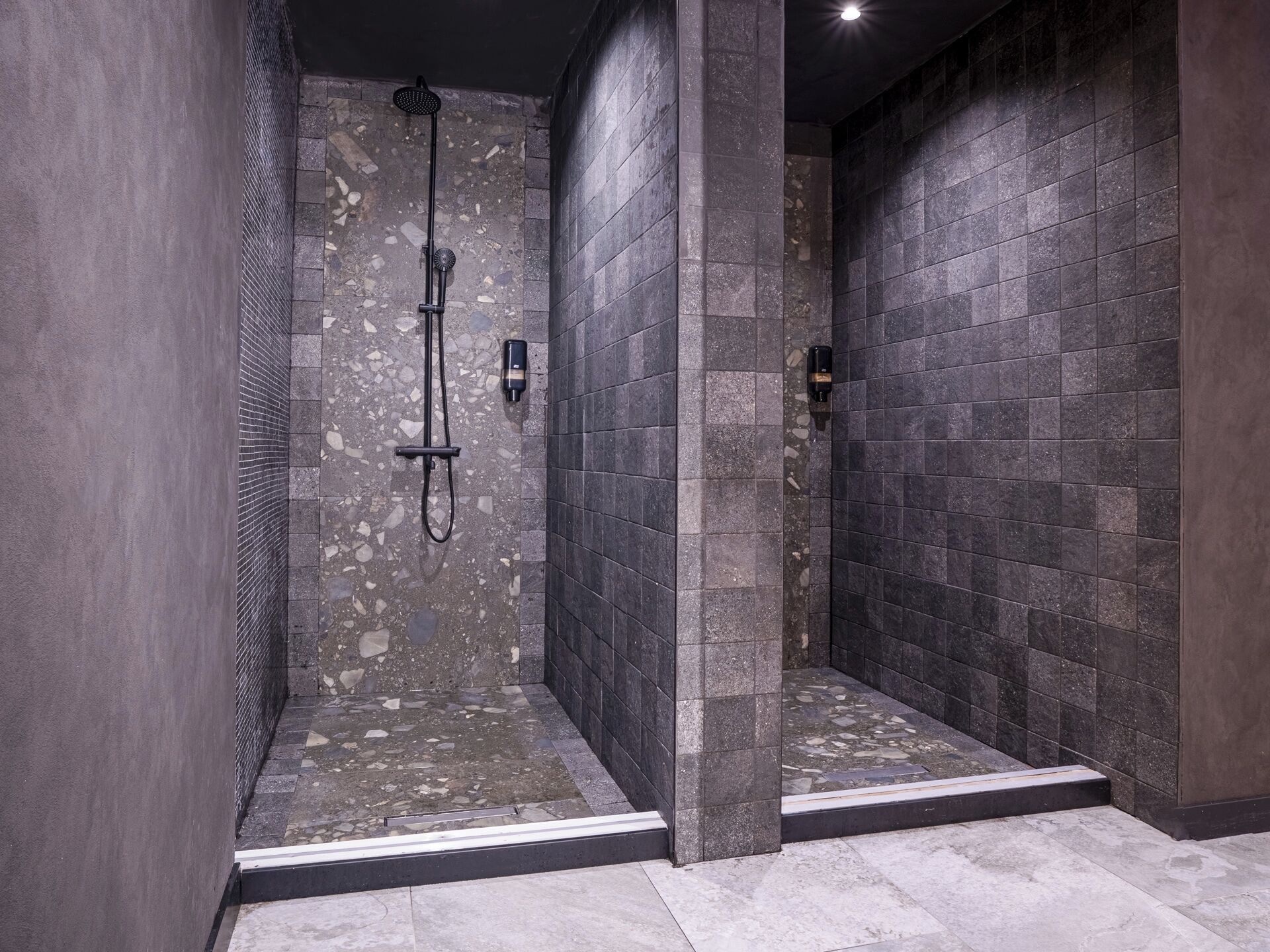 A modern shower area with a built-in rain showerhead, a handheld showerhead, and a soap dispenser on the wall.