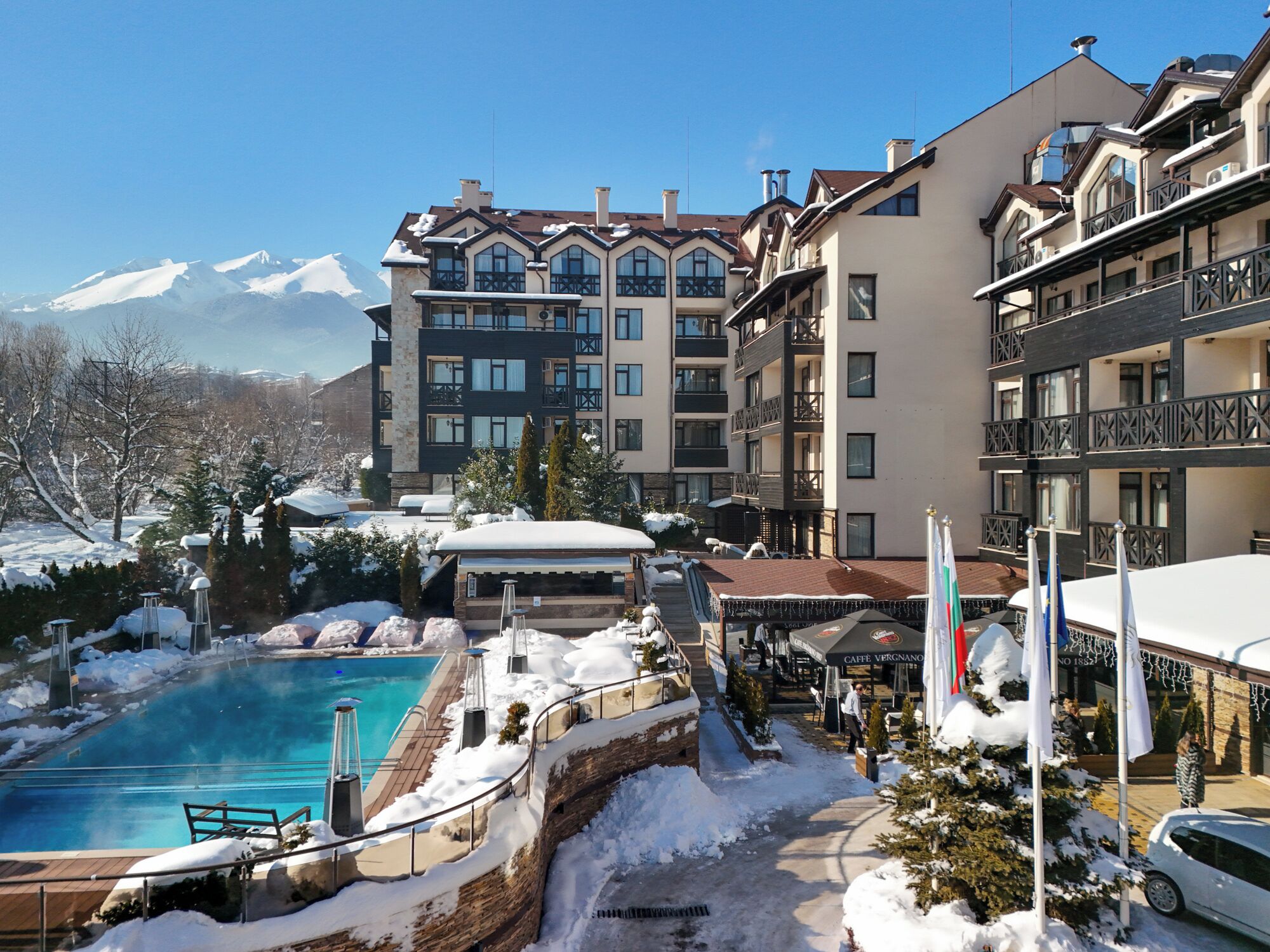 Un hotel con piscina rodeado de nieve, vistas a la montaña y varios balcones.