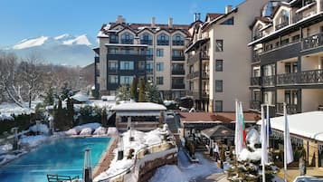 Un hotel con piscina rodeado de nieve, vistas a la montaña y varios balcones.