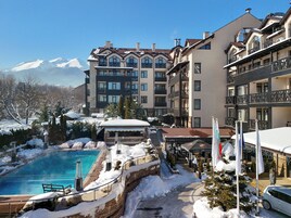 Un hotel con piscina rodeado de nieve, vistas a la montaña y varios balcones.
