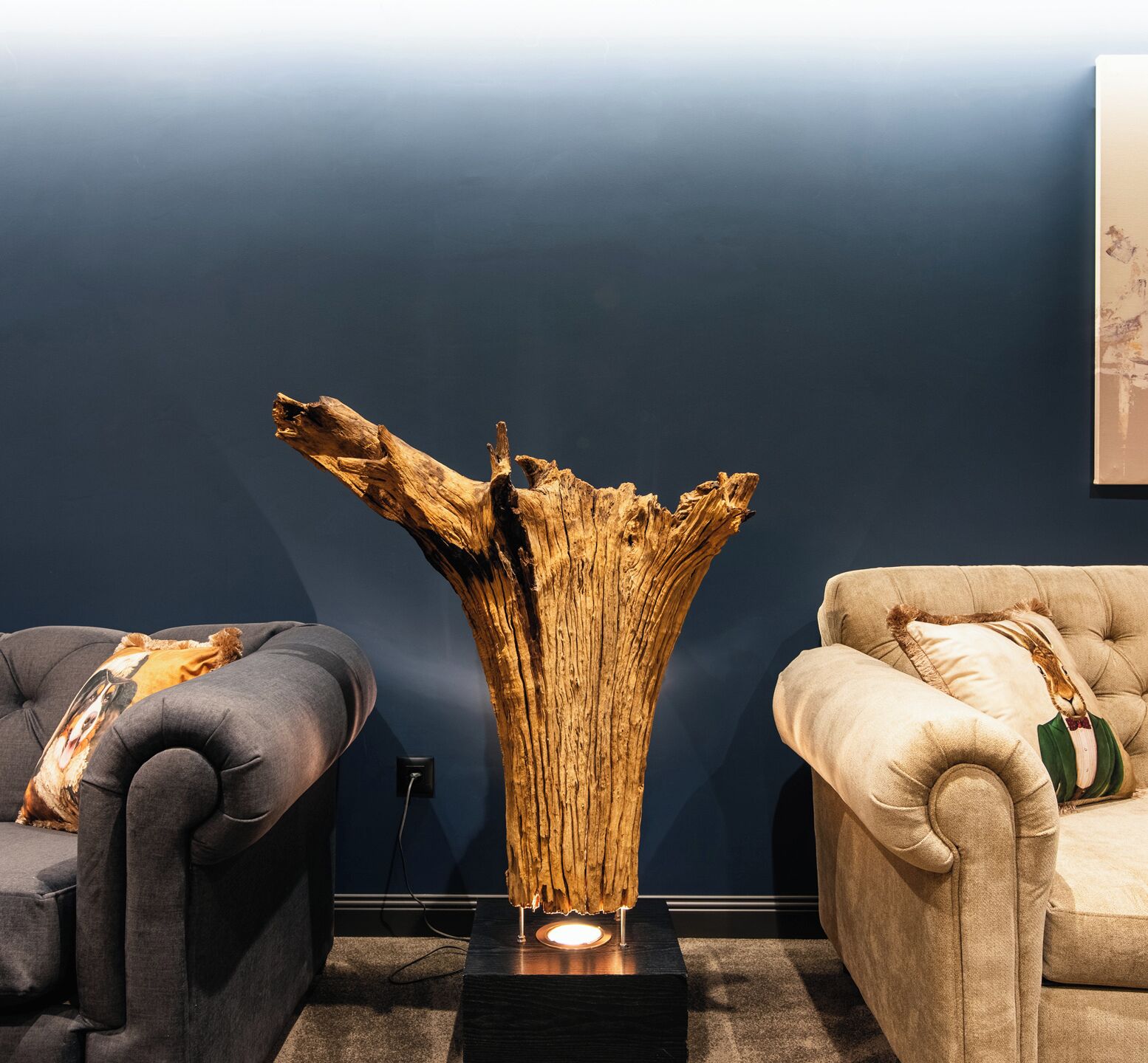 A room with two armchairs, a wooden sculpture centerpiece, and a dark blue wall.