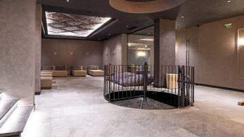 A modern spa area with a central circular seating area, a skylight, and a mirrored wall.