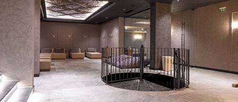 A modern spa area with a central circular seating area, a skylight, and a mirrored wall.