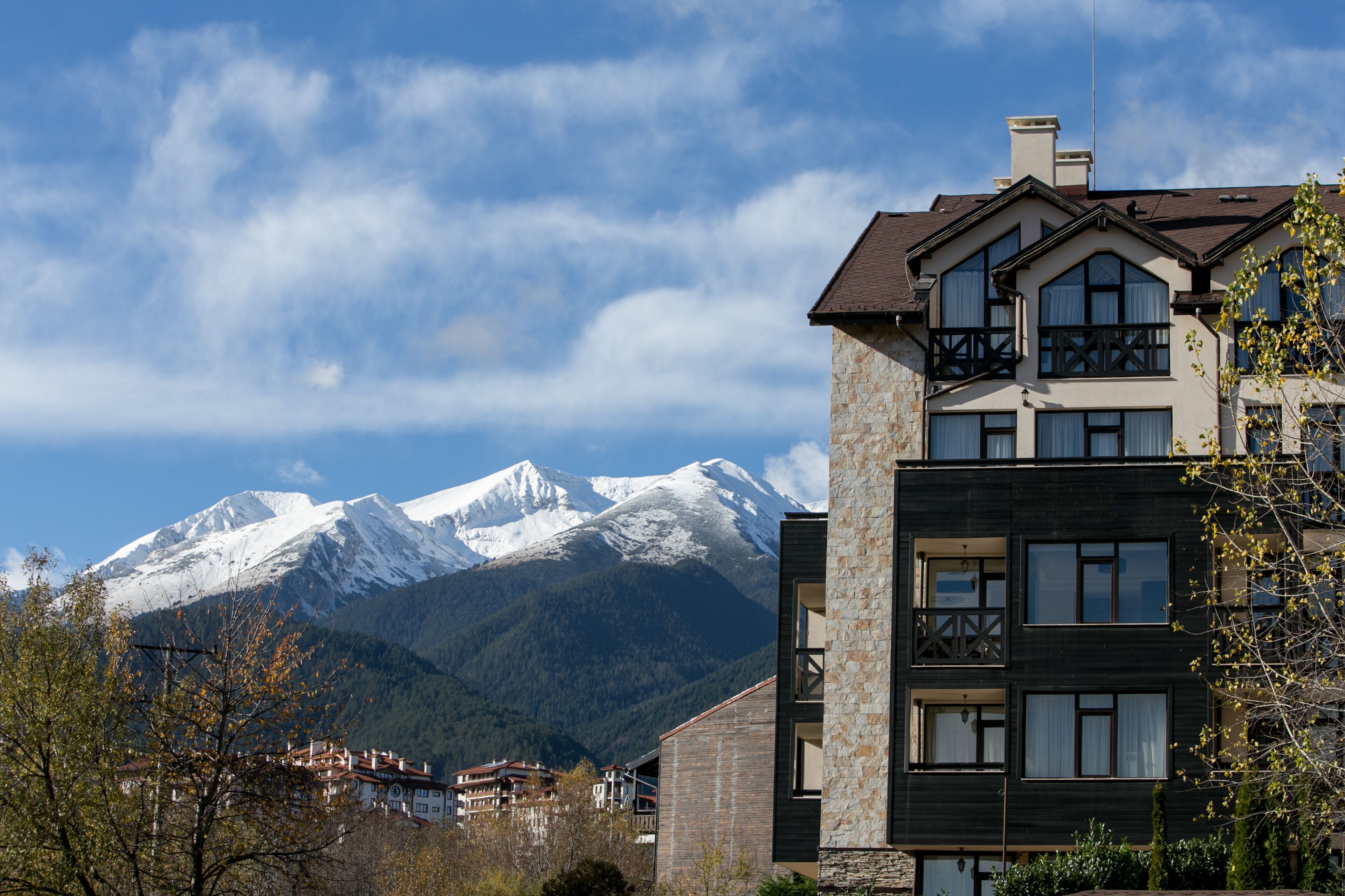 A modern building with a stone facade and multiple windows, set against a backdrop of snow-capped mountains and a clear sky.