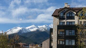 A modern building with a stone facade and multiple windows, set against a backdrop of snow-capped mountains and a clear sky.