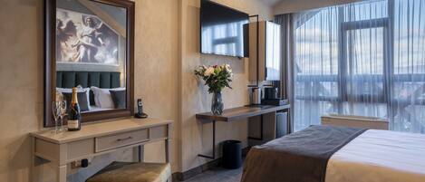 A hotel room with a bed, a desk with a chair, a TV, a window with curtains, and a painting on the wall.