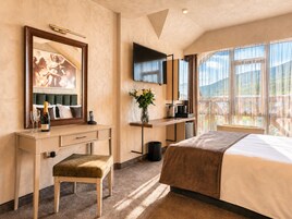 Habitación de hotel con cama, escritorio con teléfono, televisor, ventana con vista y un cuadro en la pared.
