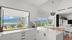 A modern kitchen with white cabinetry, a large island, and a view of a lake and mountains.