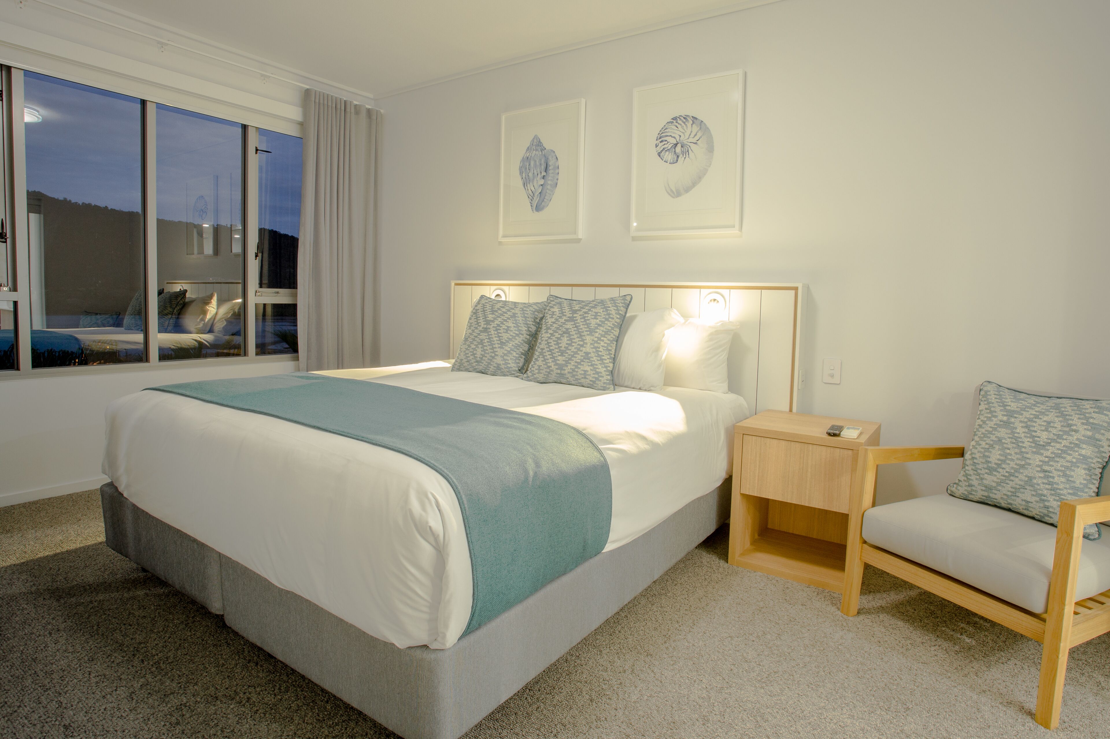 A neatly arranged bedroom with a large bed, bedside tables, a chair, and framed artwork on the wall.