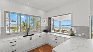 A modern kitchen with white cabinetry, a black sink, and large windows offering a view of a beach and palm trees.