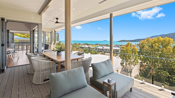 A spacious balcony with a view of the sea and mountains, furnished with wicker chairs and a sofa.