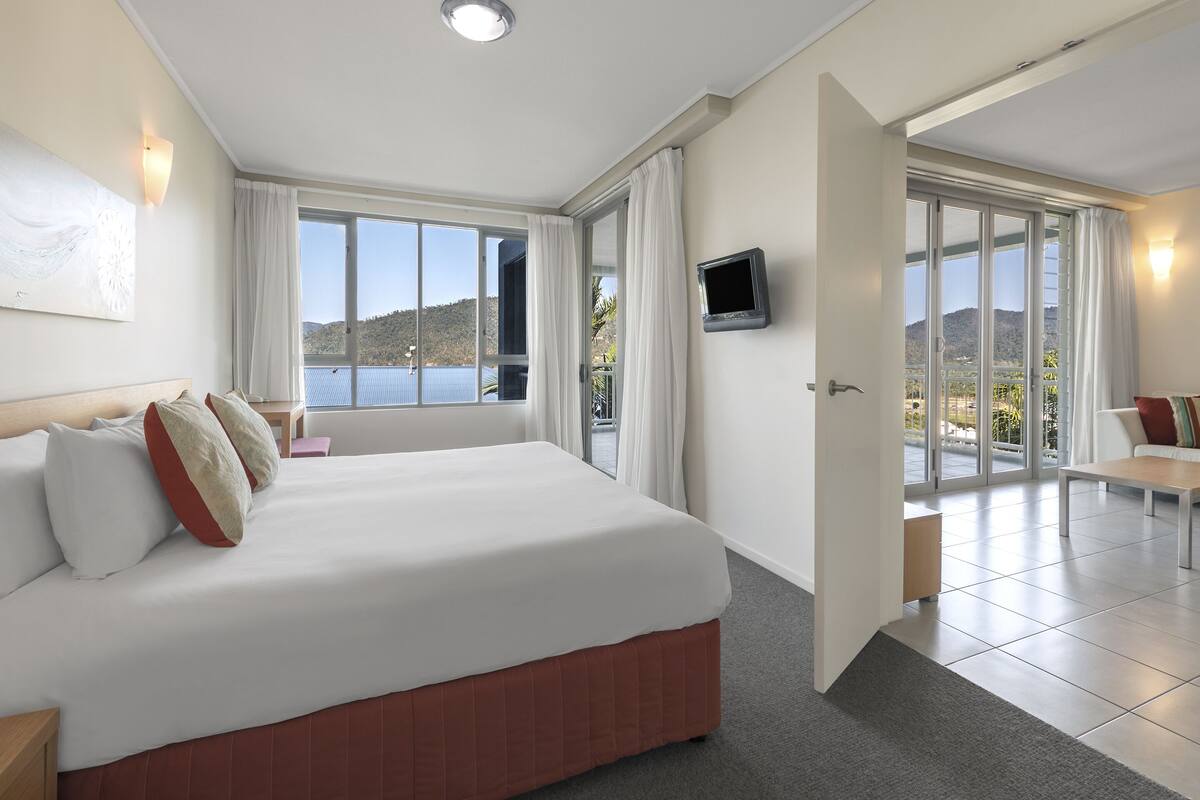 Habitación de hotel con una cama grande, televisión y balcón con vista al mar.