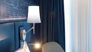 A modern hotel room with a bed, a nightstand, a lamp, a chair, and a large window with curtains. - Hôtel Mercure Toulon La Seyne-Sur-Mer (La Seyne-sur-Mer)