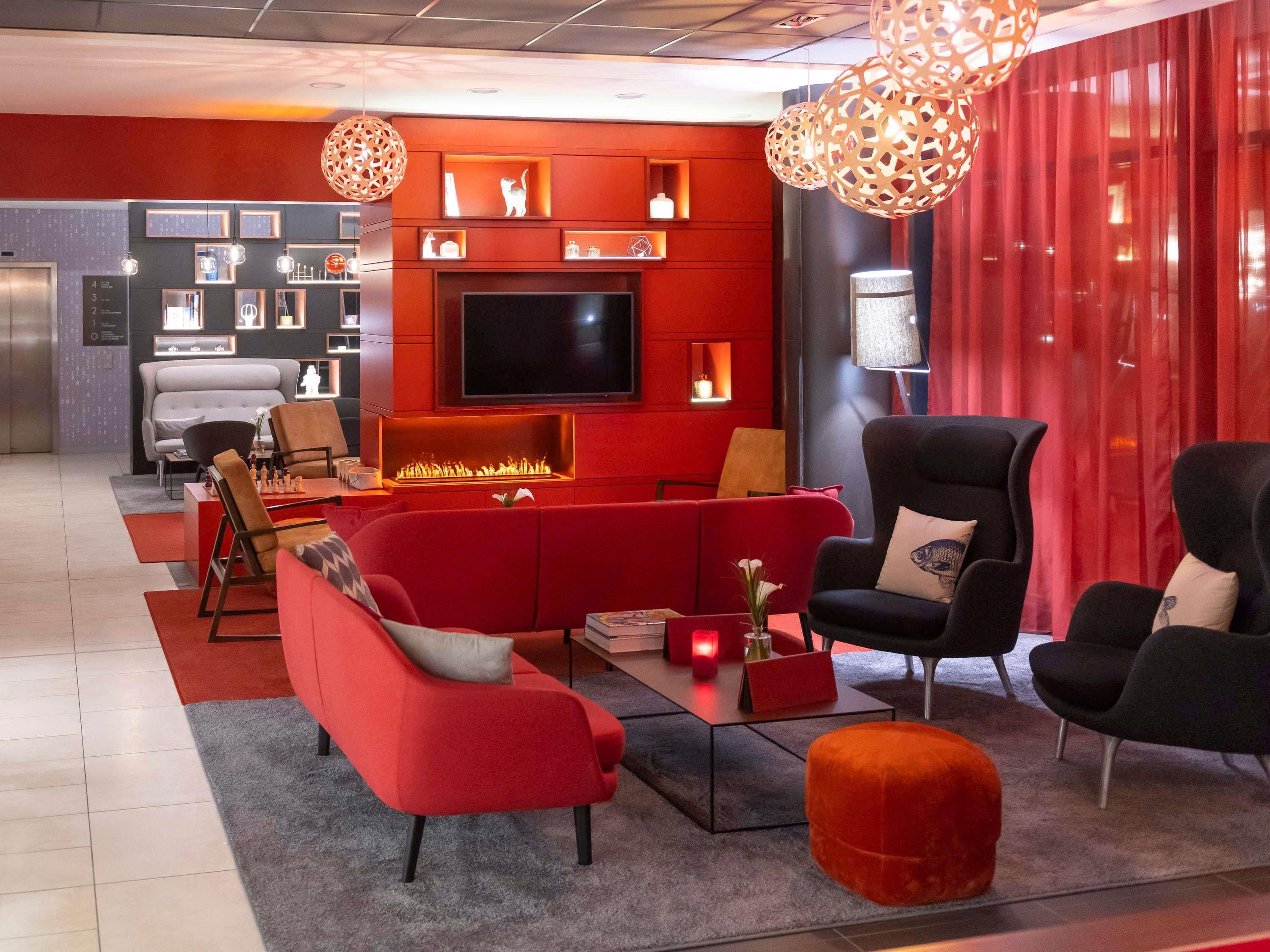 A modern living room with a red sofa, black armchairs, a fireplace, and a flat-screen TV.