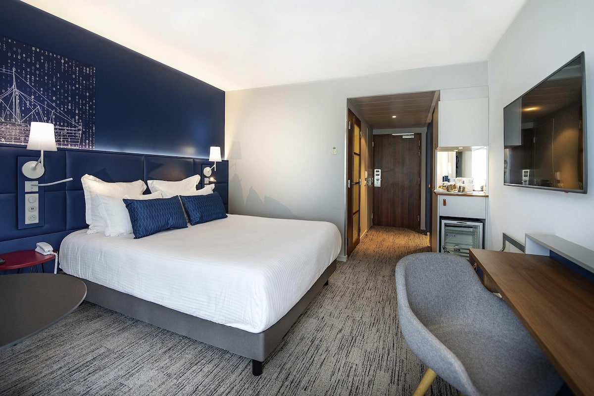 Une chambre d’hôtel avec un lit, une table de chevet, une lampe et une vue sur le couloir.