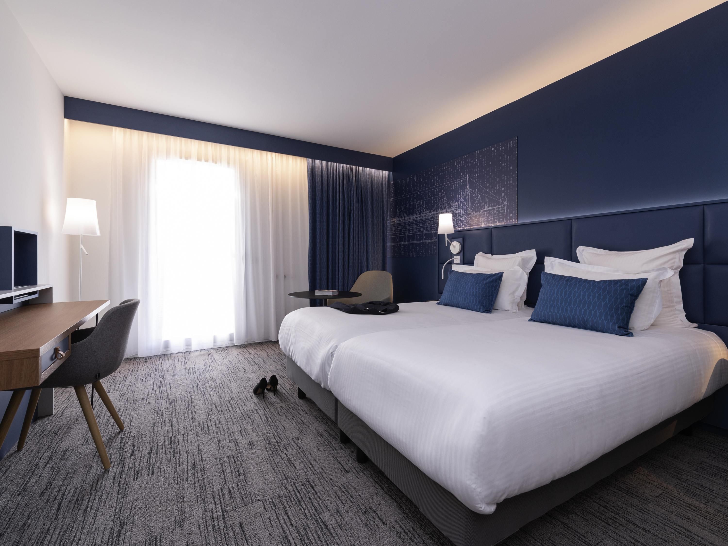Een hotelkamer met een groot bed, een bureau met stoel, een televisie en een raam met gordijnen.