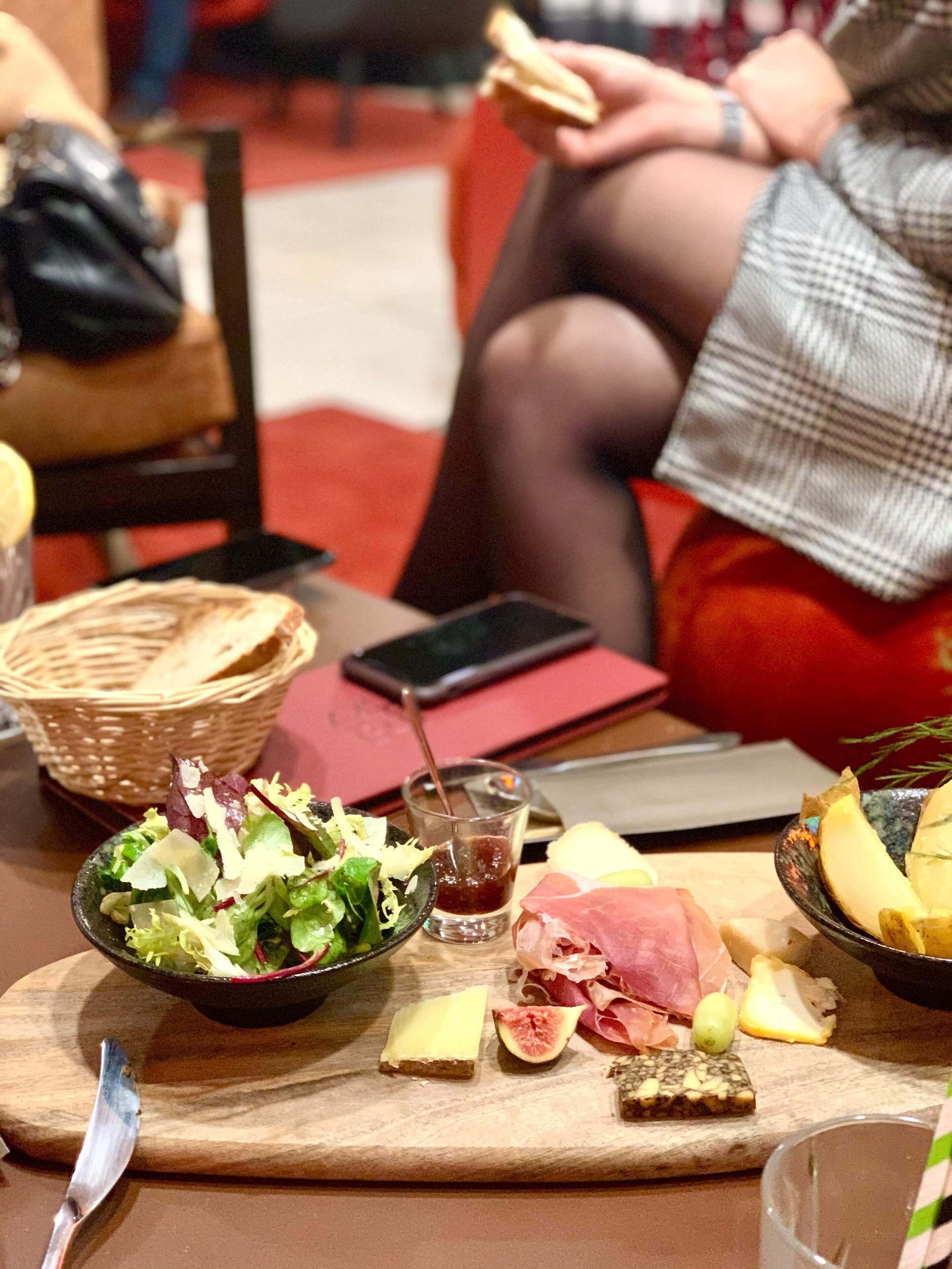 Una mesa con ensalada, queso, carnes y una bebida.