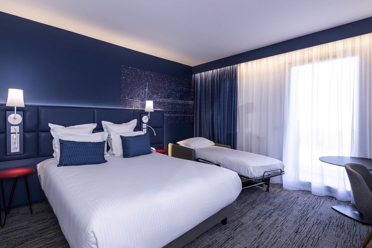Una habitación de hotel con una cama grande, dos mesitas de noche, un escritorio y una silla.
