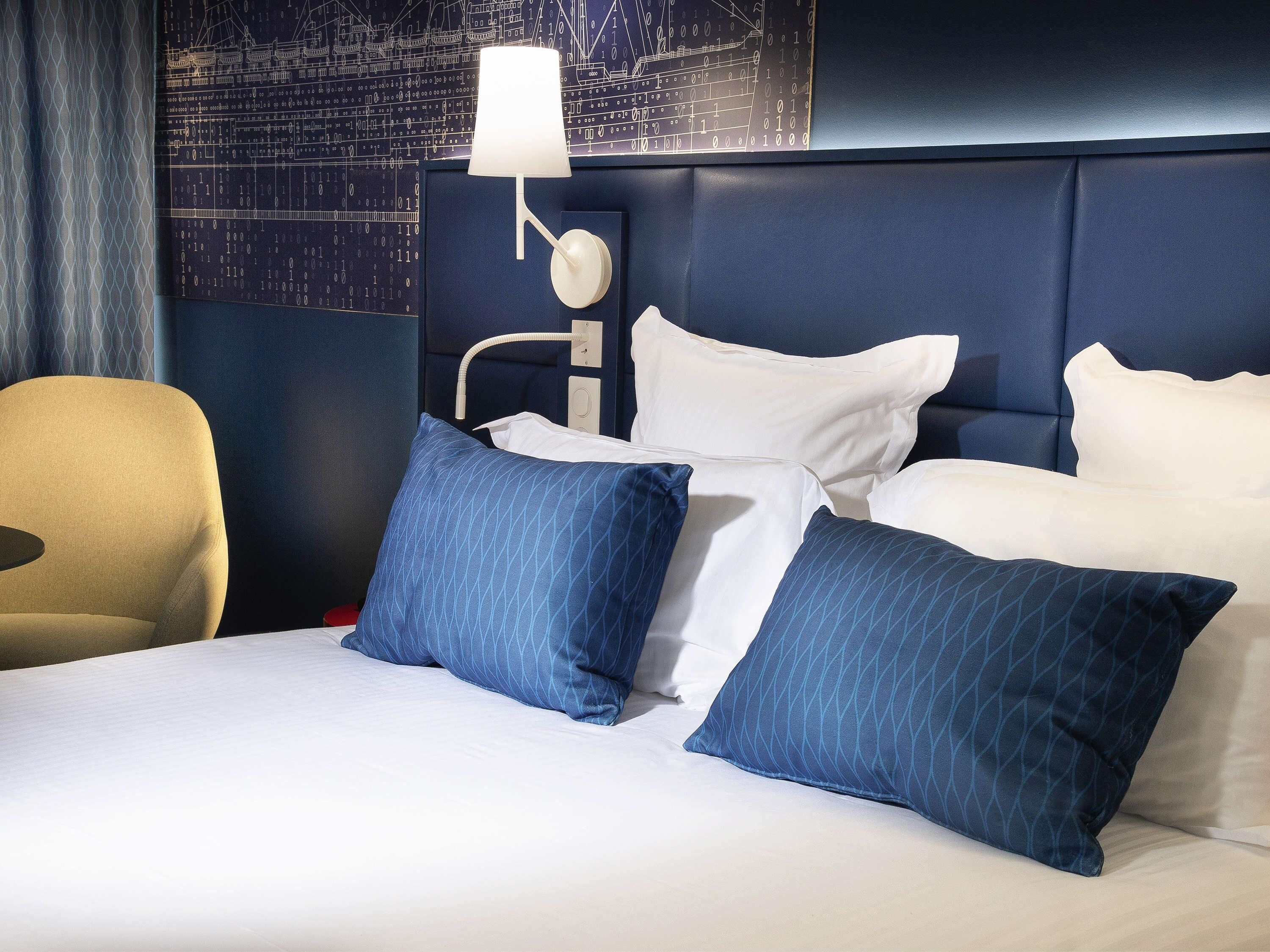 Una habitación de hotel con una cama, almohadas, una lámpara y una pared con diseño de placa de circuito.