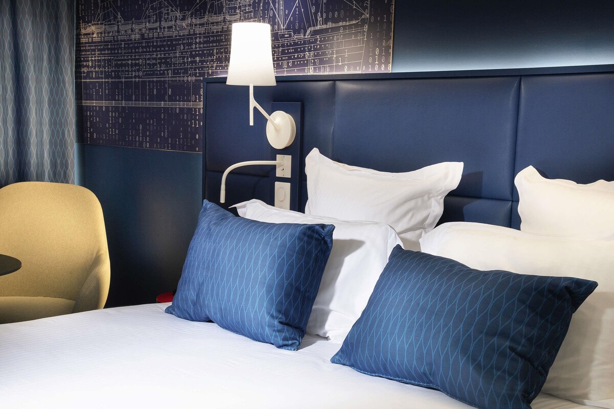 Habitación de hotel con cama, almohadas, lámpara y pared con diseño de placa de circuito.