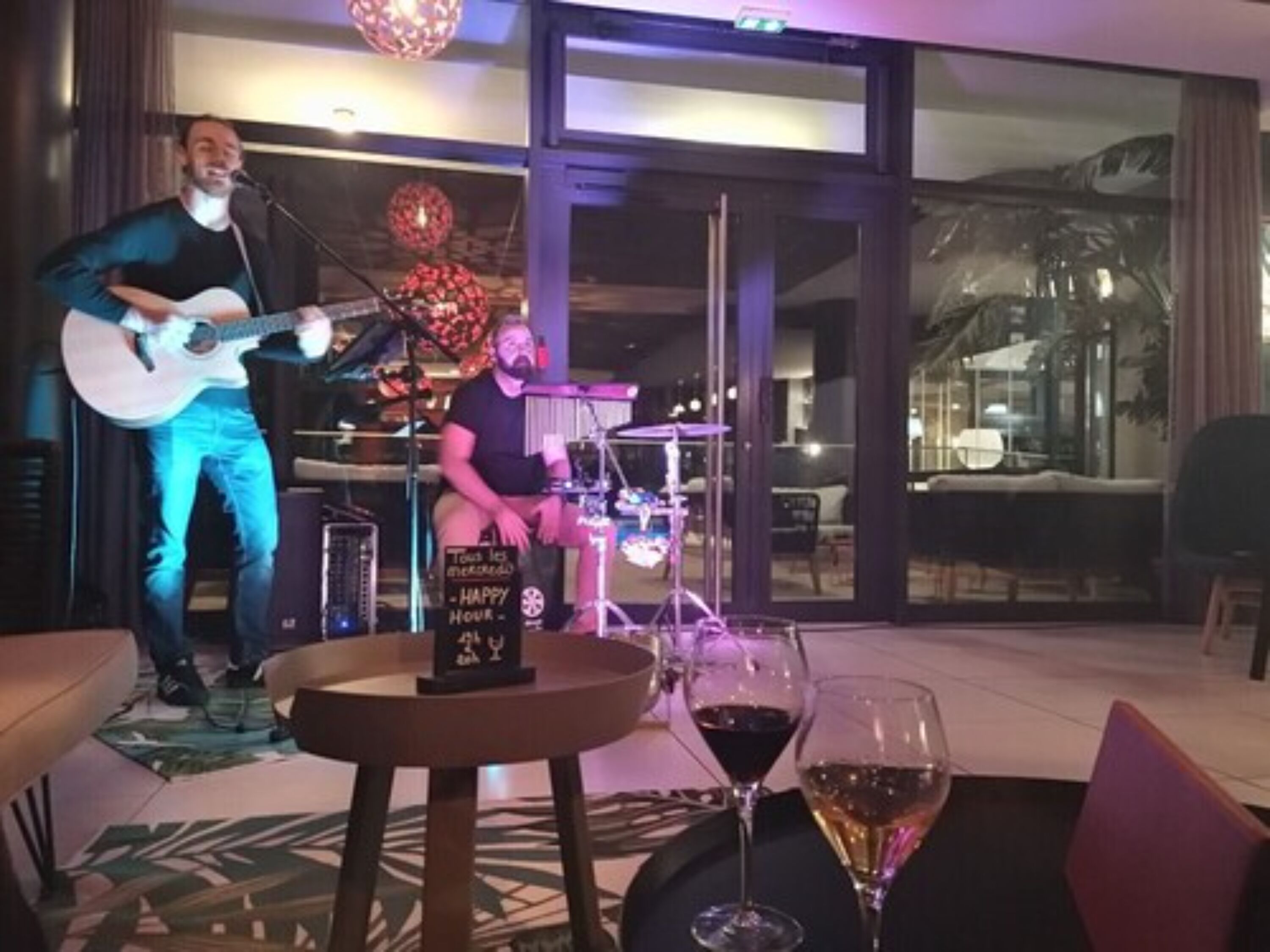 A musician playing a guitar on a stage with a sign that reads "Happy Hour."