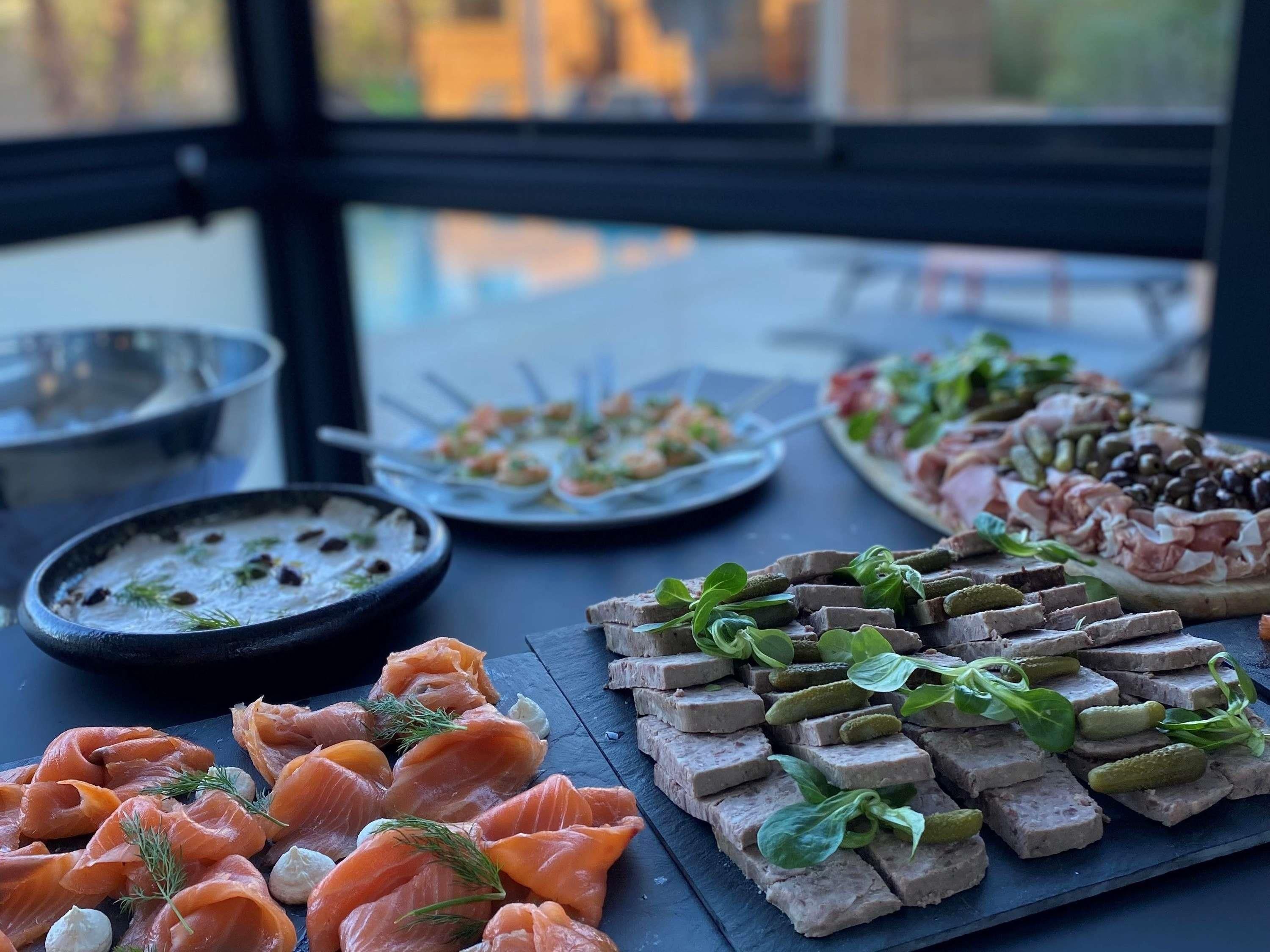 Ett urval av olika matvaror som står uppradade på ett bord, bland annat rökt lax, paté och andra smårätter.