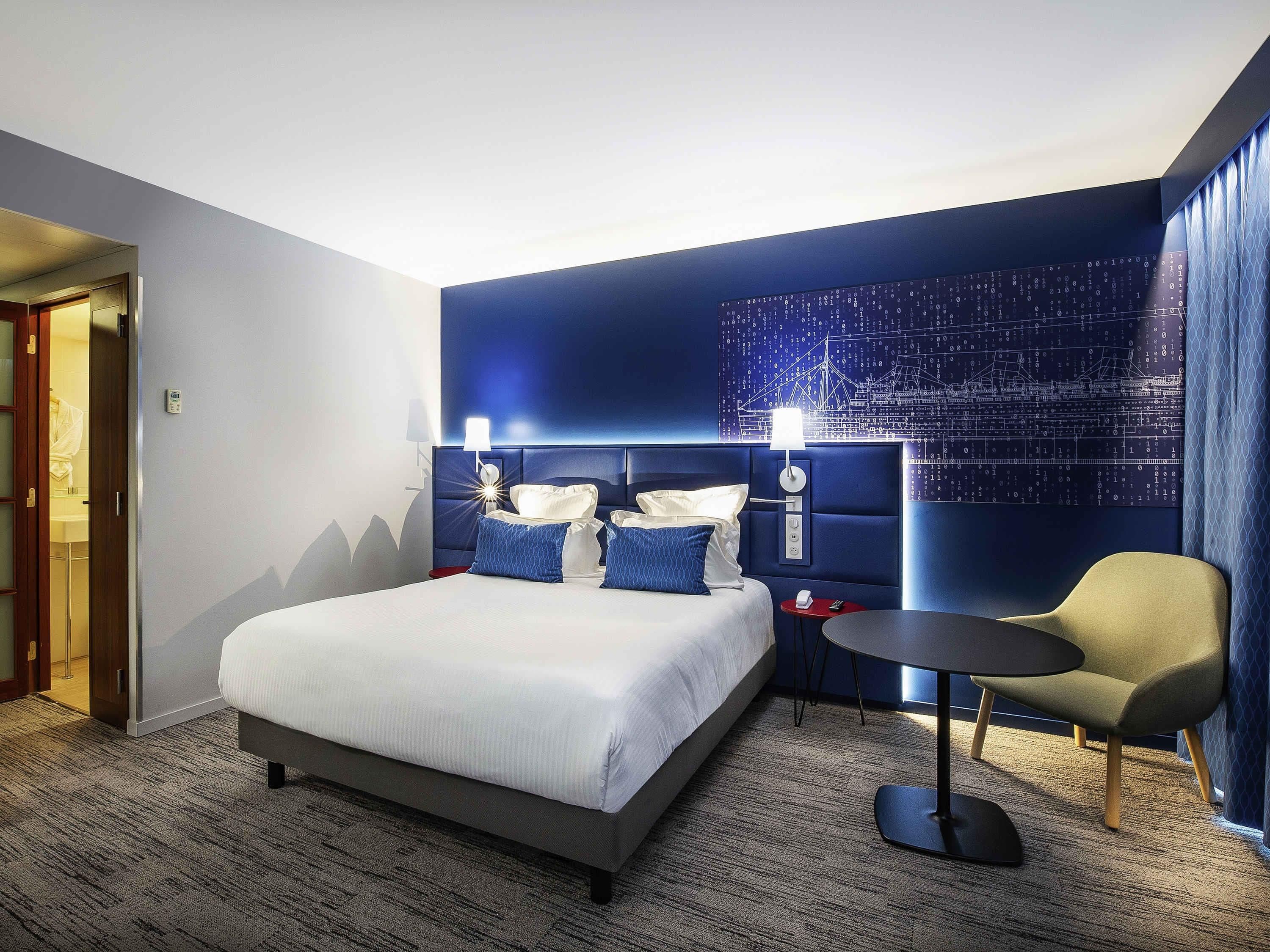 Una habitación de hotel con cama, mesitas de noche, una silla y una pared con diseño digital.