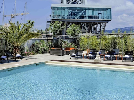 A swimming pool with lounge chairs and a modern building with a glass facade.. Hôtel Mercure Toulon La Seyne-Sur-Mer