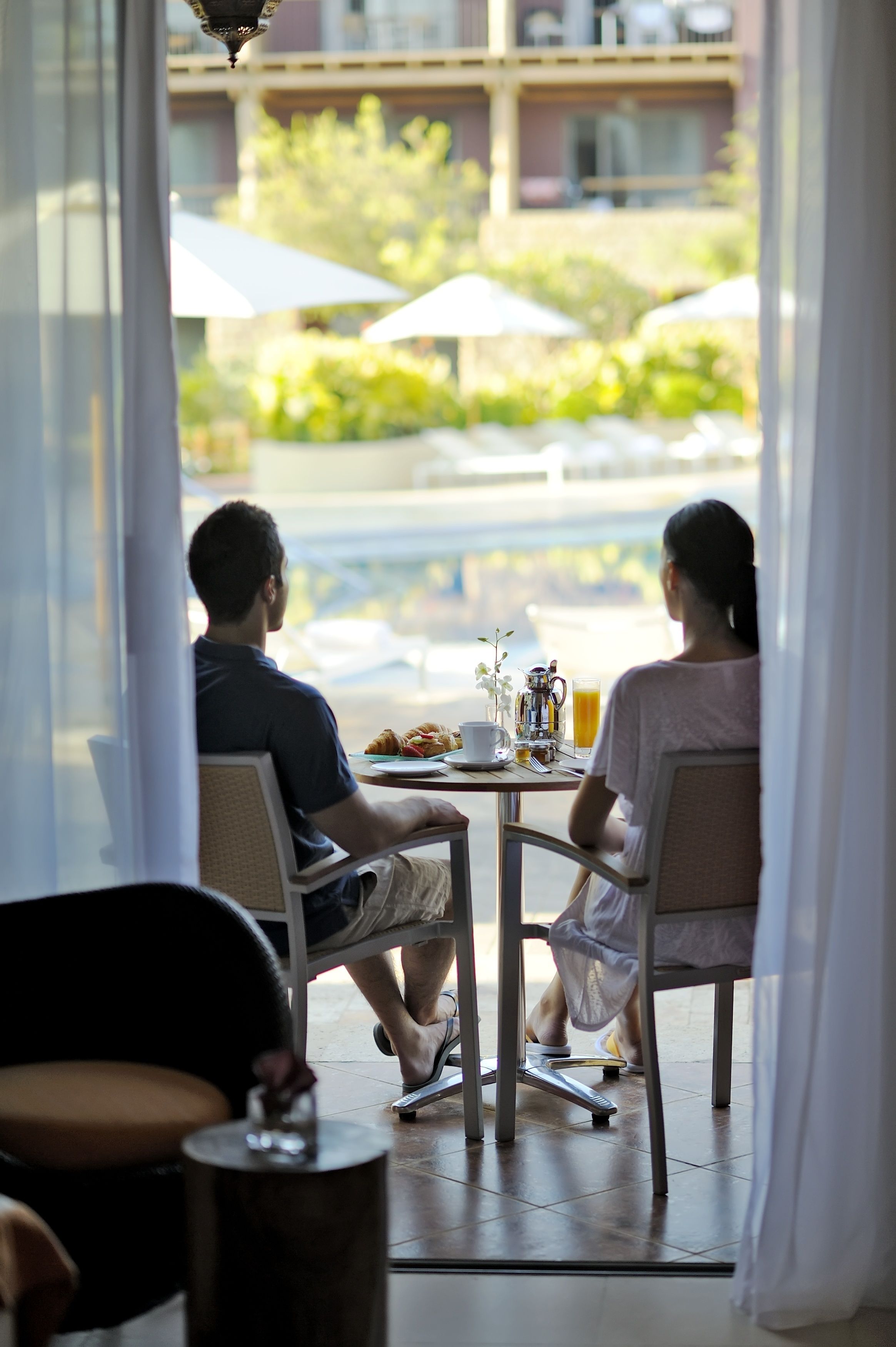 A couple dining at a table with a view of a pool and greenery outside.