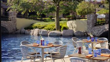 Outdoor seating by a pool with stone walls and greenery.