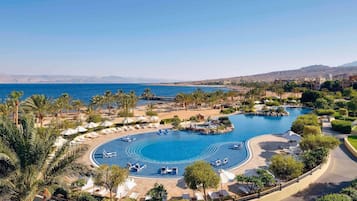 Un complexe hôtelier doté d’une grande piscine circulaire, de palmiers et offrant une vue sur la mer.
