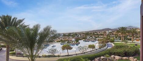 Un resort amb una gran piscina, palmeres i un paisatge de muntanyes al fons.