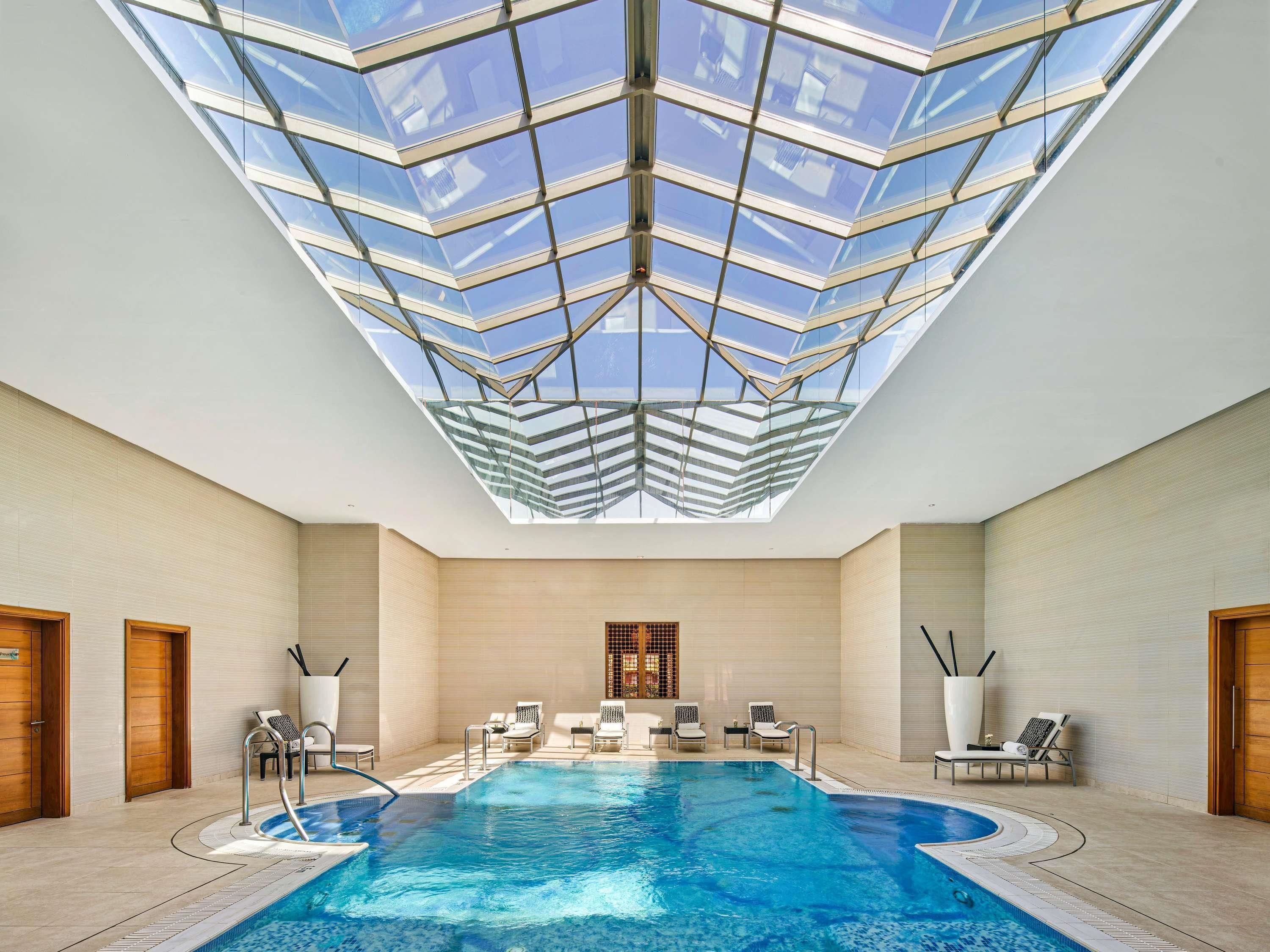 A swimming pool with a glass ceiling, lounge chairs, and wooden doors.