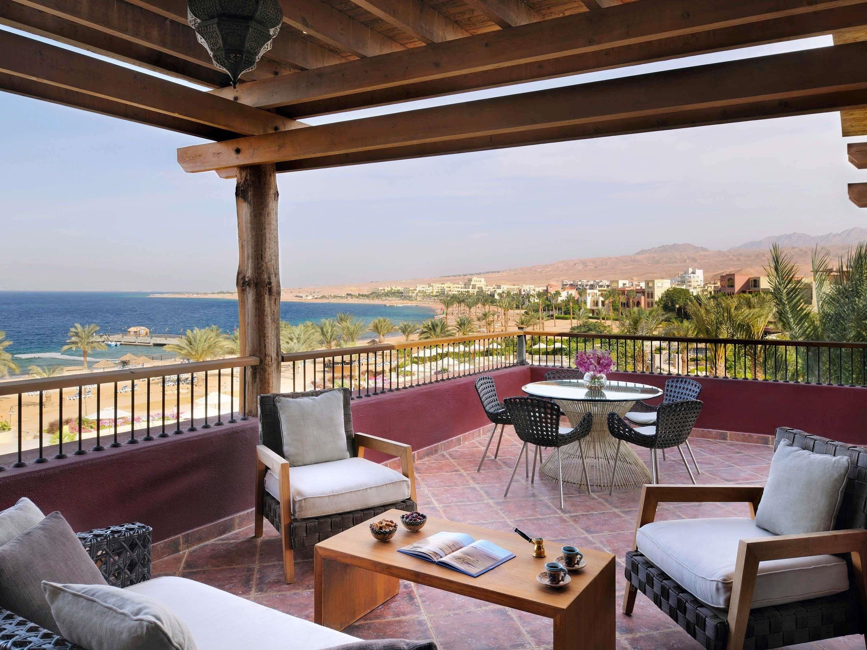 A balcony with a view of the sea, wooden furniture, and a table with a book and teacups.