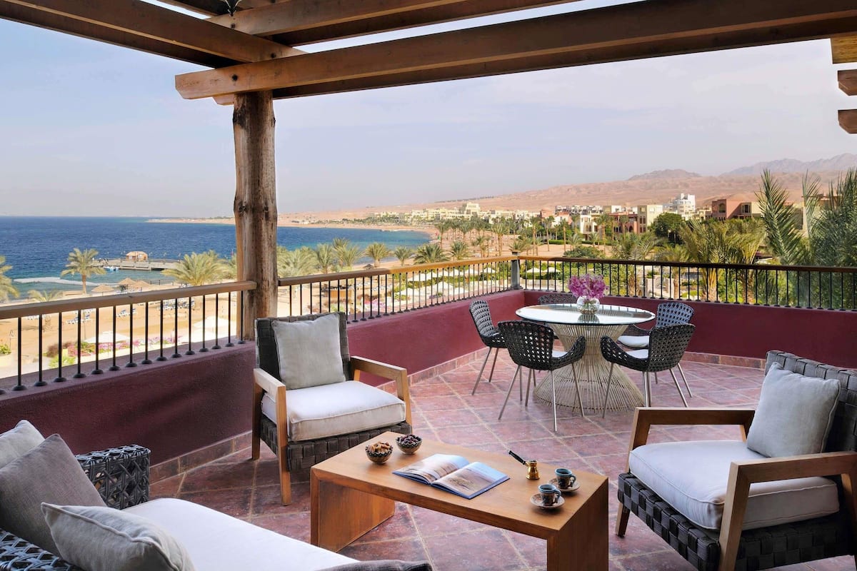 A balcony with a view of the sea, wooden furniture, and a table with a book and teacups.