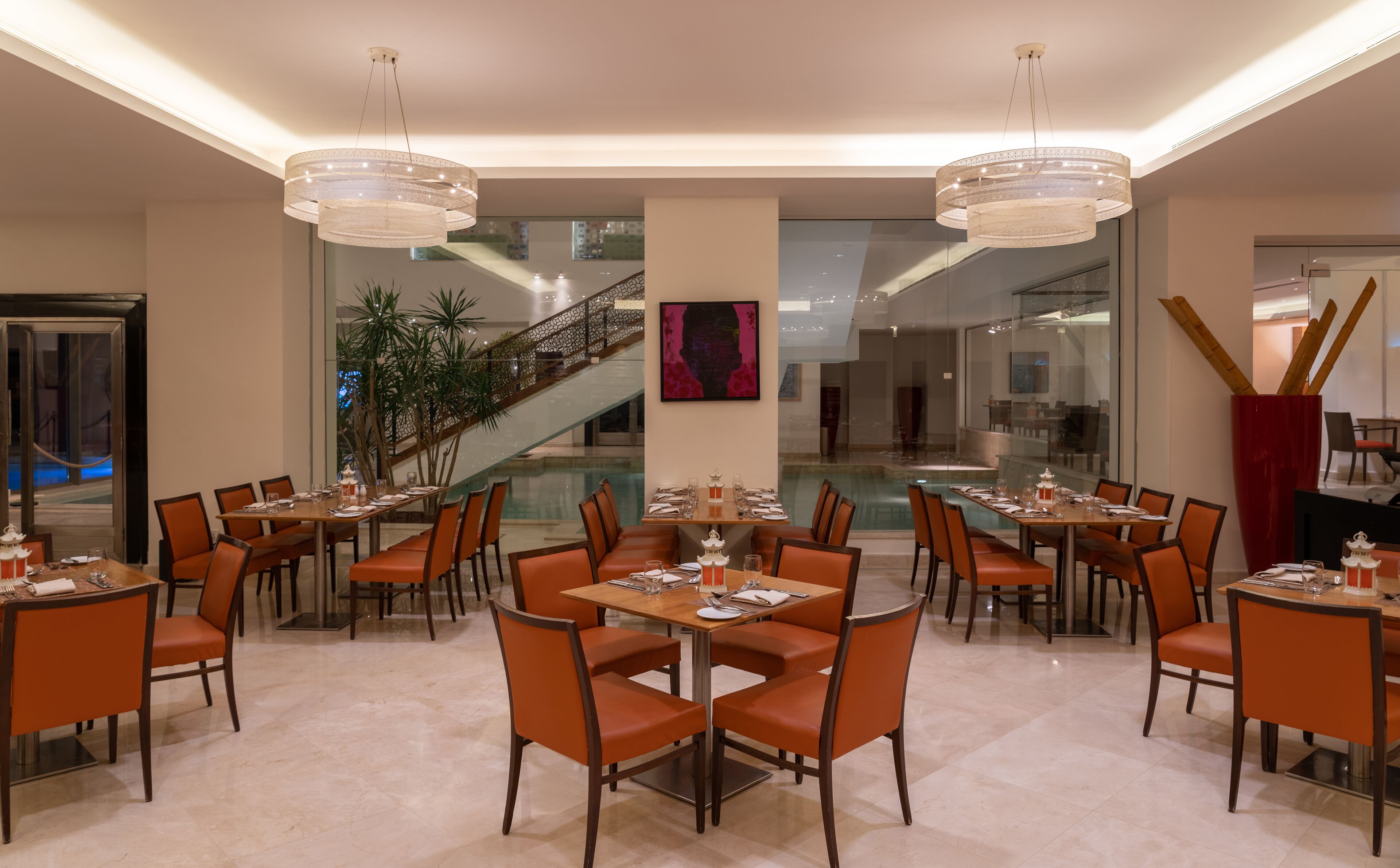 Zona pranzo moderna con diversi tavoli e sedie, un grande lampadario e una scala che conduce a un livello superiore.