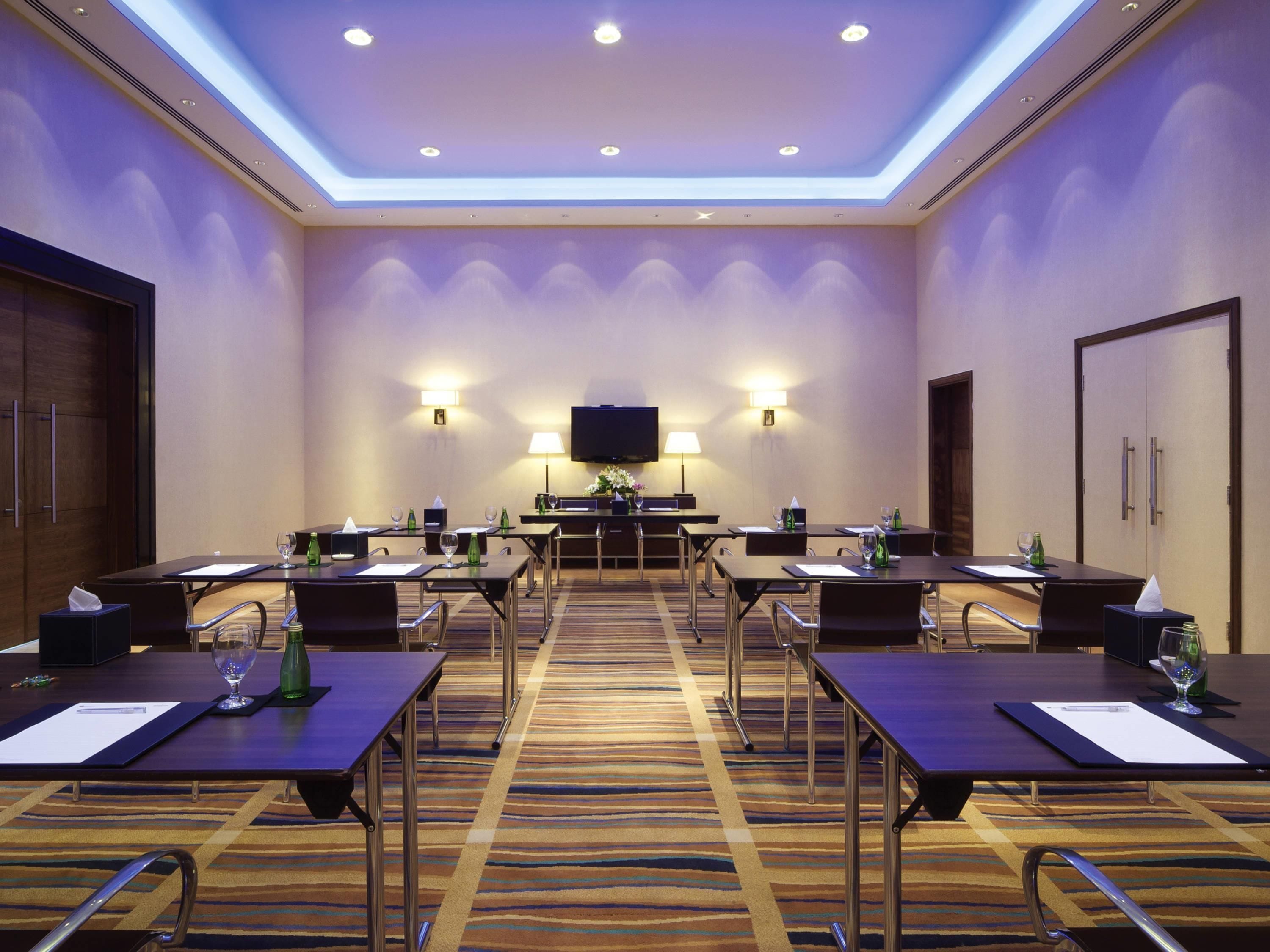 A conference room with multiple tables, chairs, a flat-screen TV, and wall-mounted lamps.