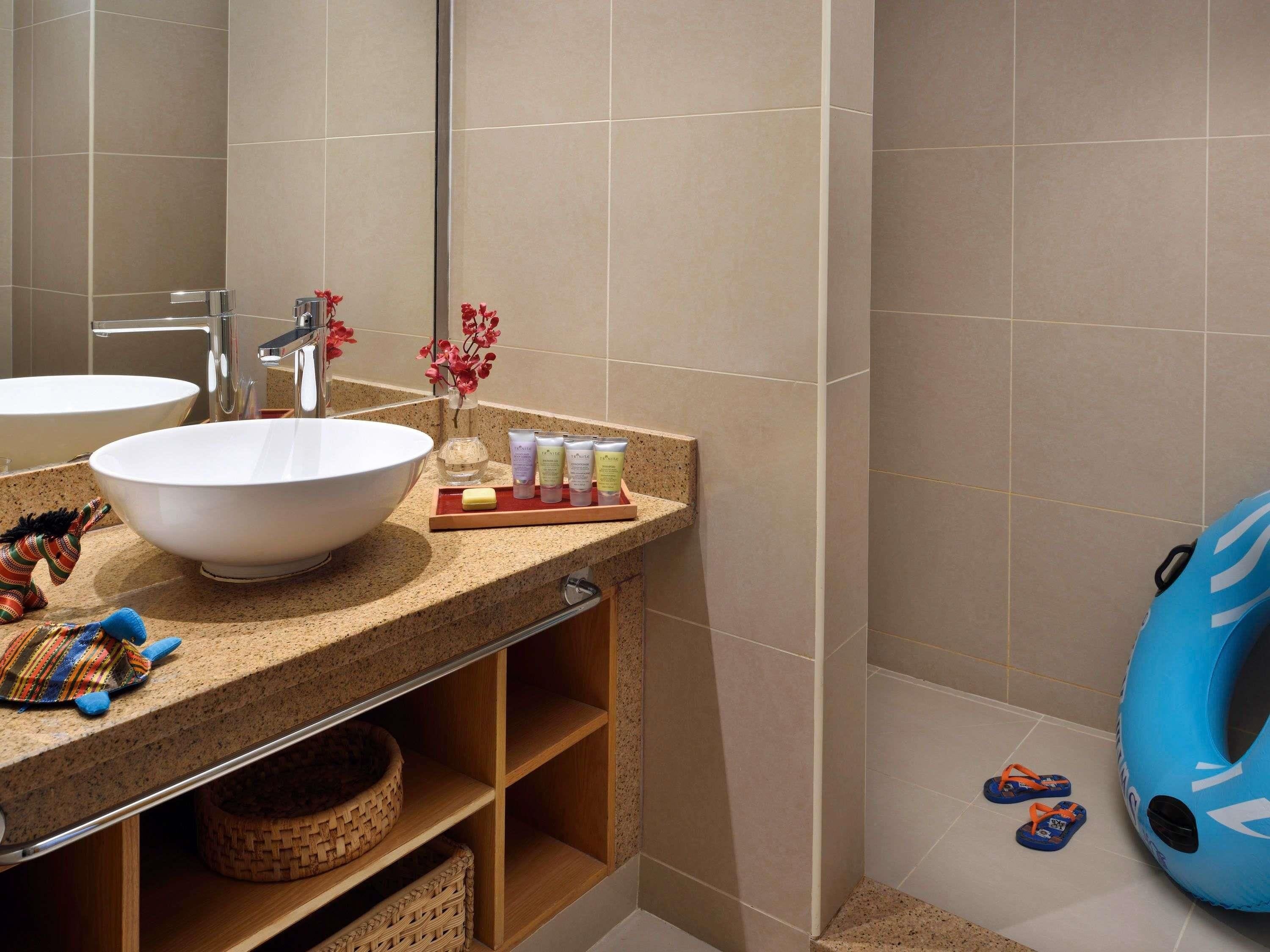A bathroom with two sinks, a mirror, a shelf with toiletries, and a blue bath ring.