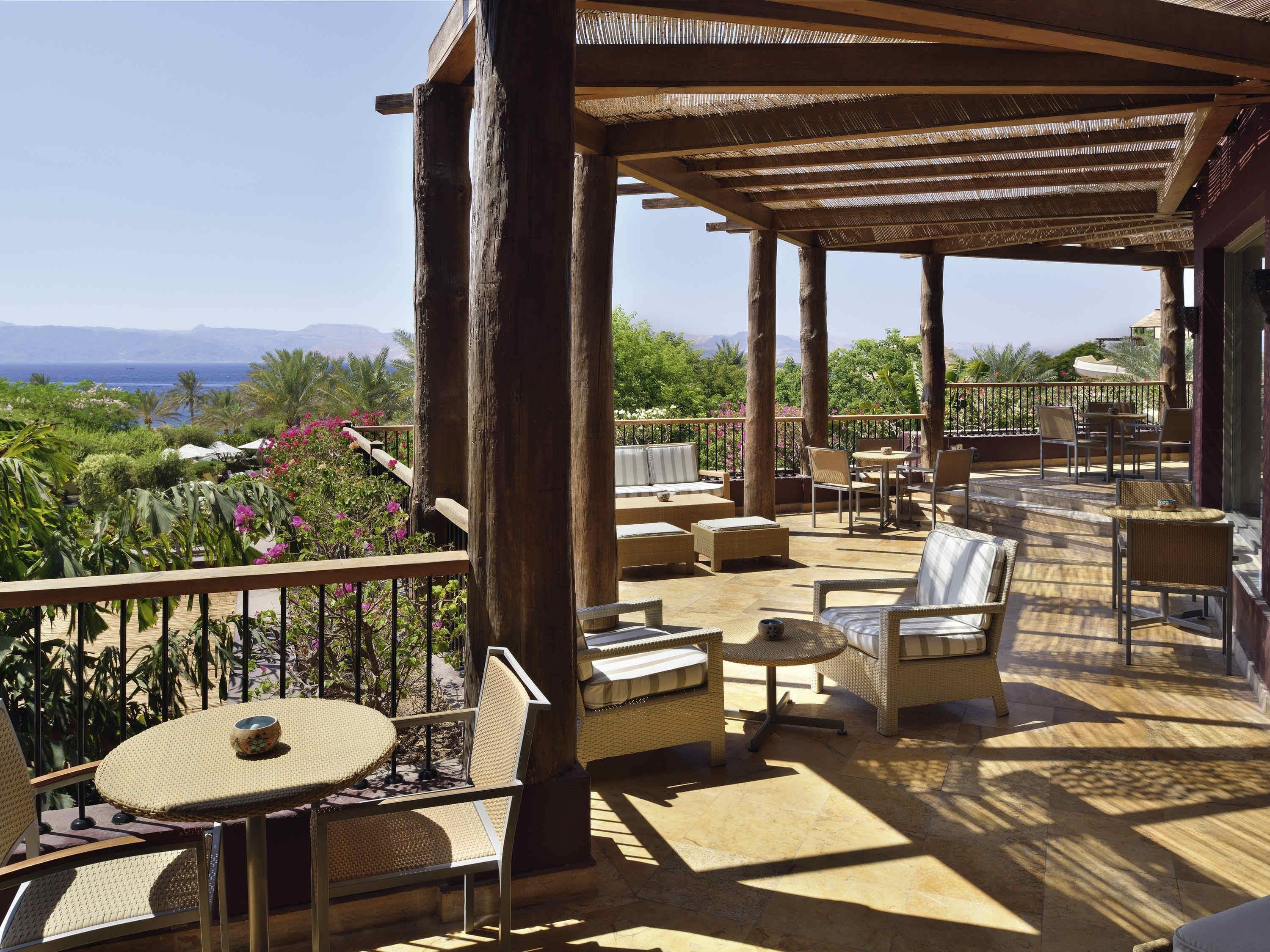 A covered outdoor seating area with wicker furniture, a pergola, and a view of the sea and mountains.