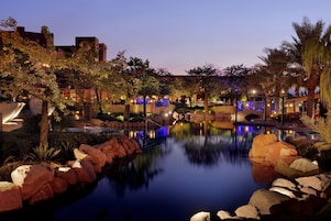 A serene hotel courtyard with a reflective pool, large rocks, and illuminated pathways.