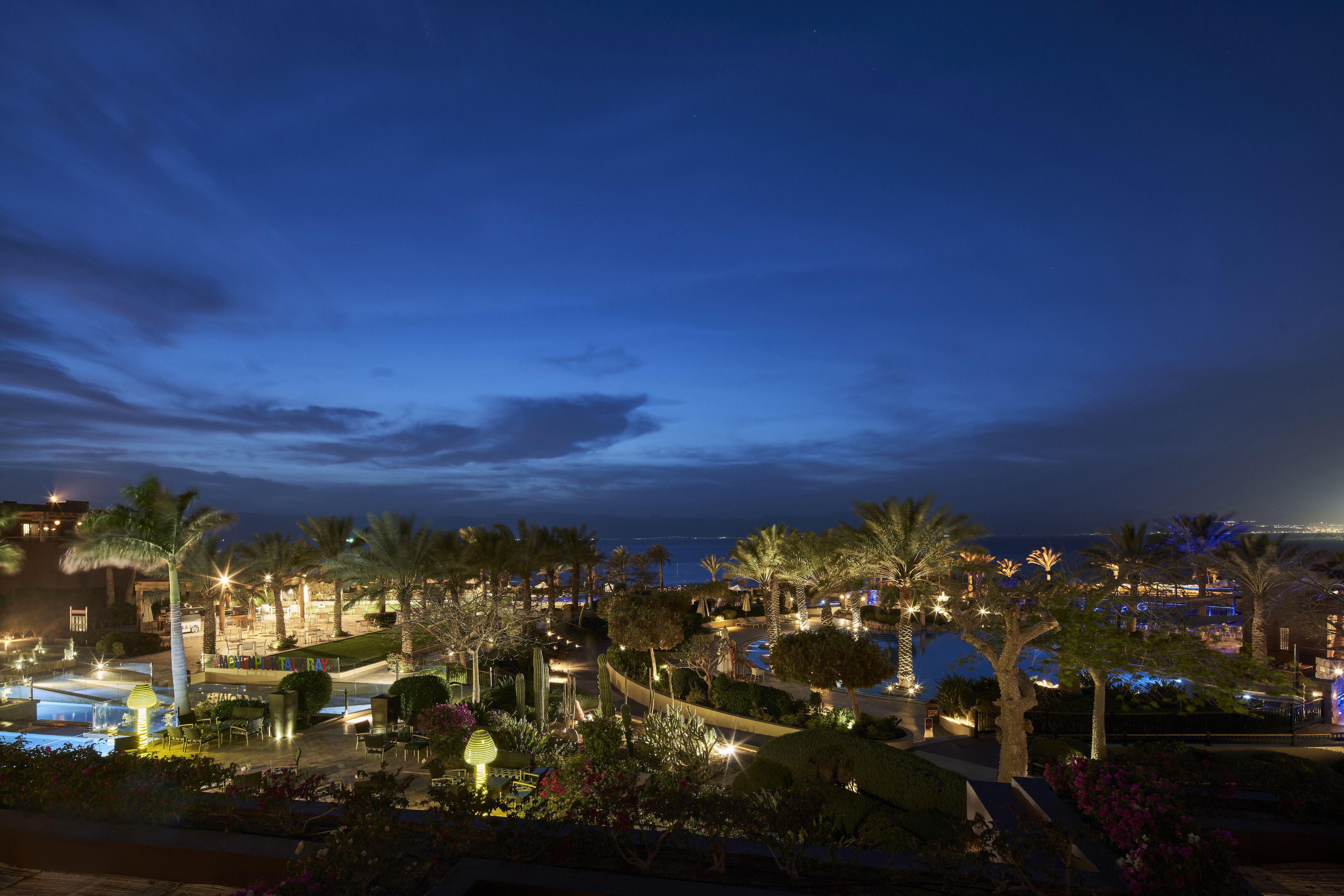 Un resort con piscina, palmeras y vista al mar de noche.