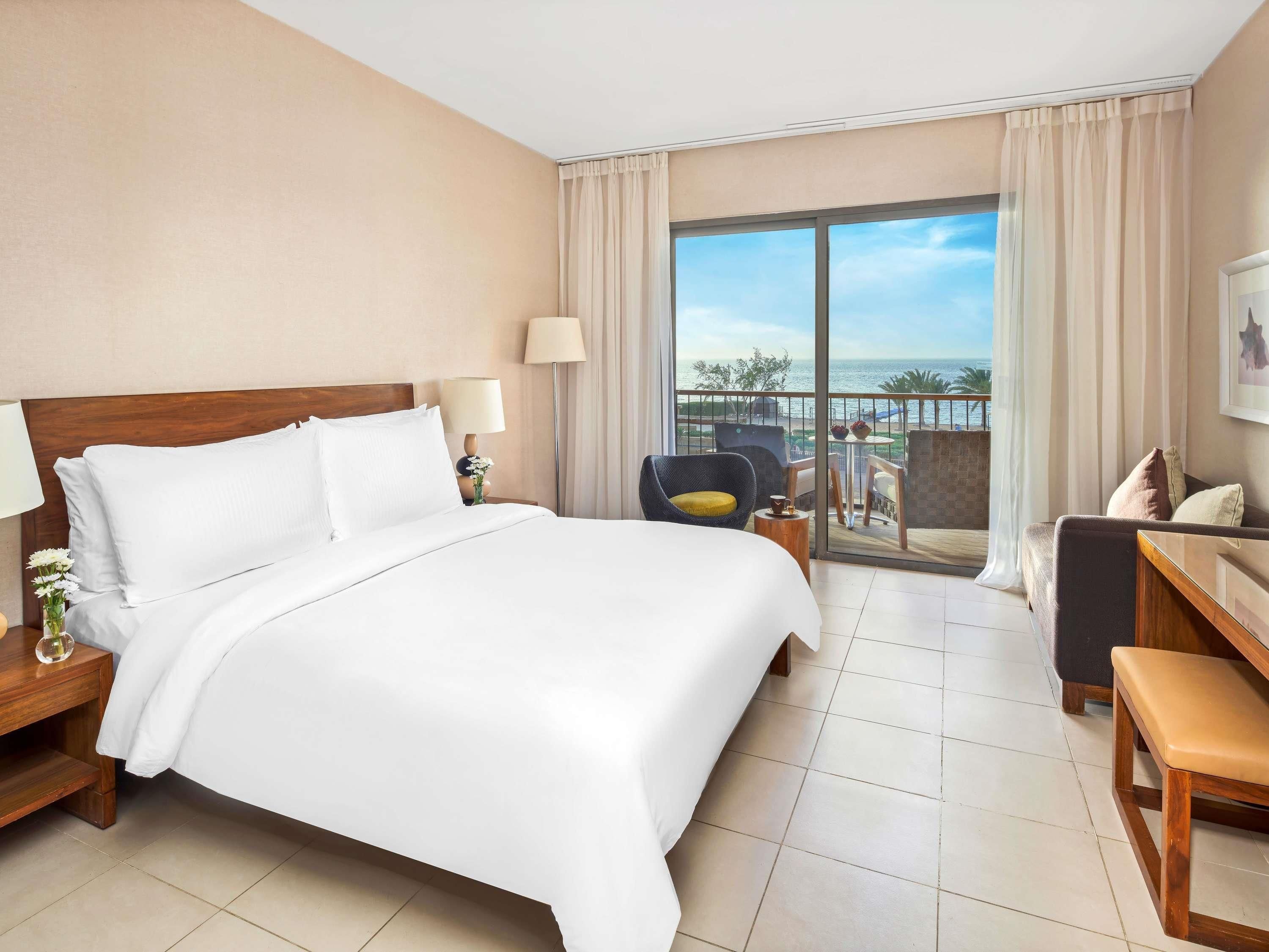 Habitación de hotel con una cama grande, un escritorio, una silla y un balcón con vista al mar.
