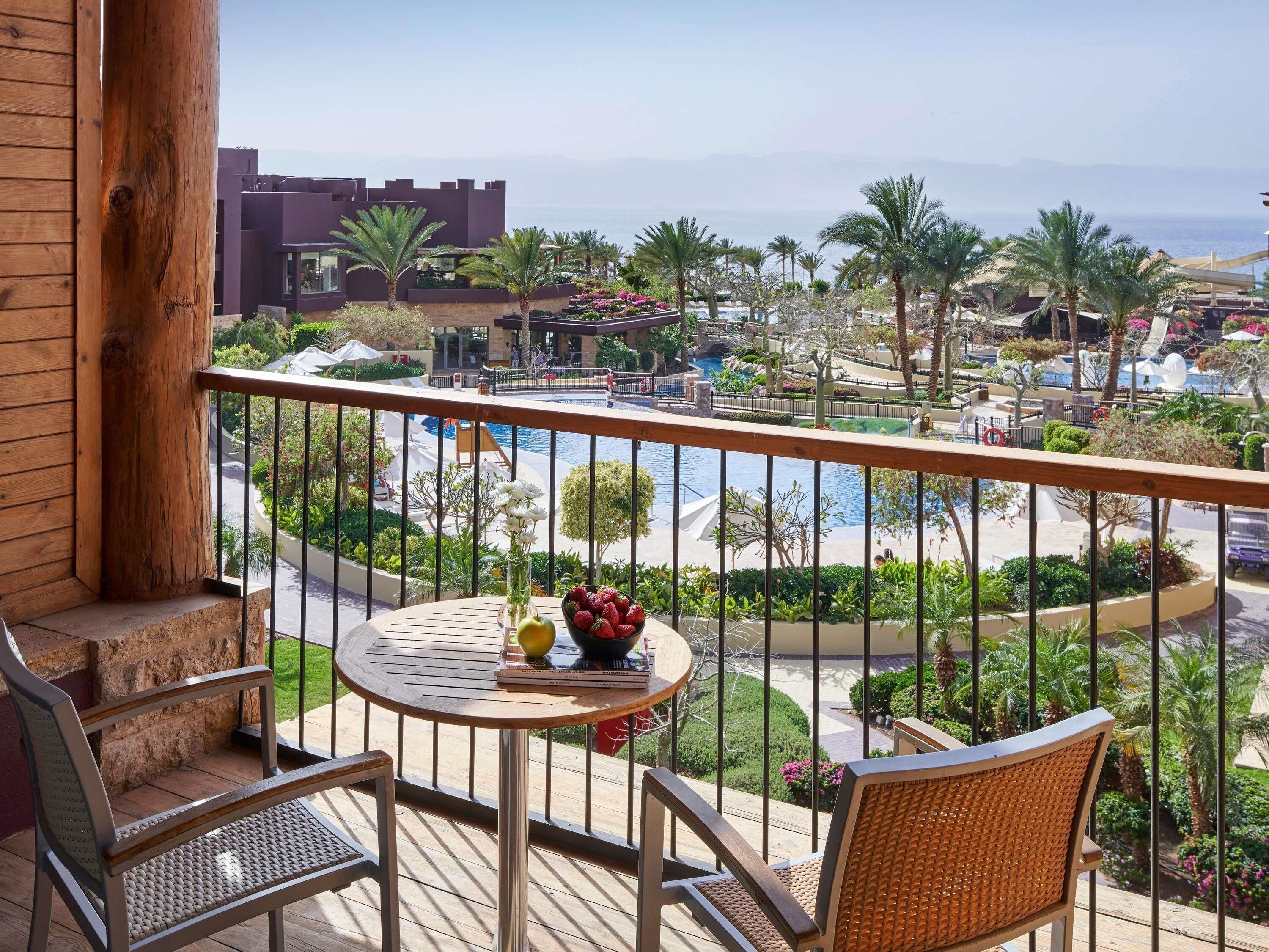 A balcony with a table, chairs, and a view of a resort pool and palm trees.