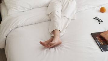A person lying on a bed with white bedding, reading a book.