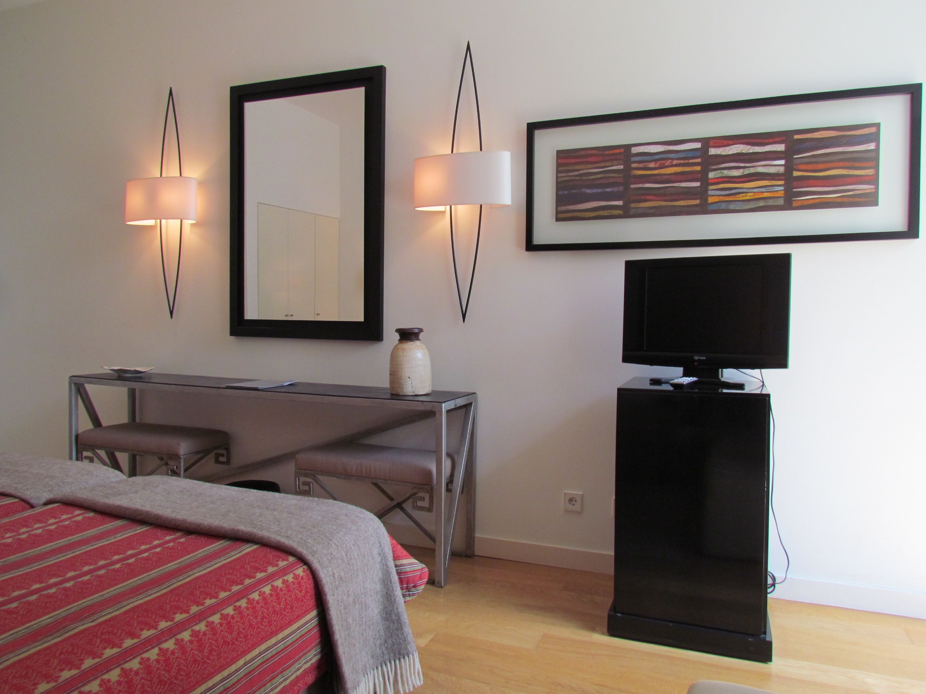 Une chambre d’hôtel comprenant un lit, un bureau avec une chaise, une télévision, un miroir et une œuvre d’art encadrée accrochée au mur.