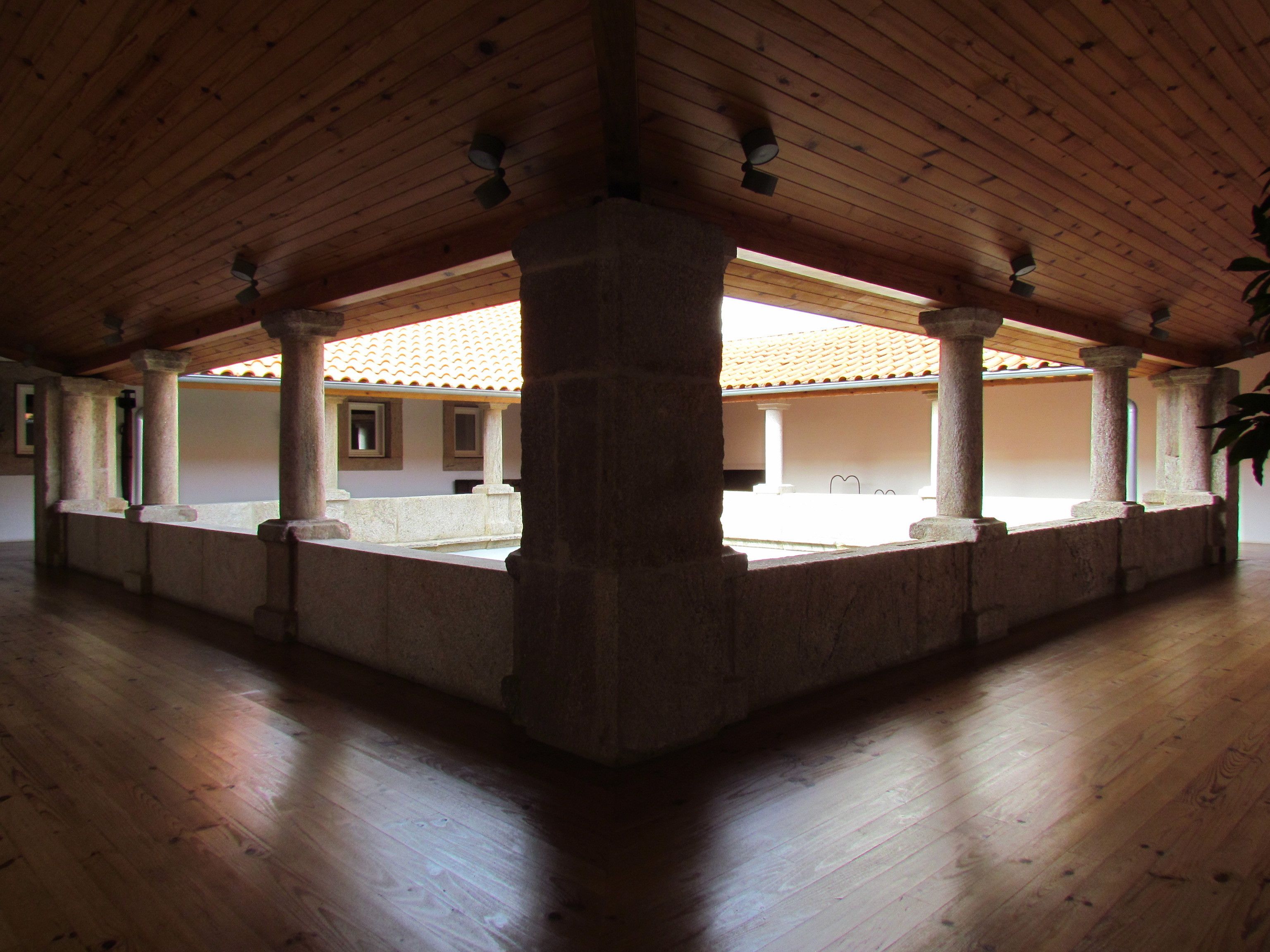 Ein geräumiger Saal mit hohen Holzbalkendecken und Säulen, einem Ziegeldach und einem Holzboden.